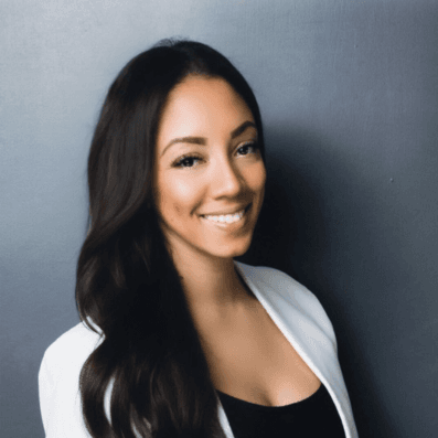 Woman with long black hair wearing a white blazer over a black top, smiling at camera against gray background