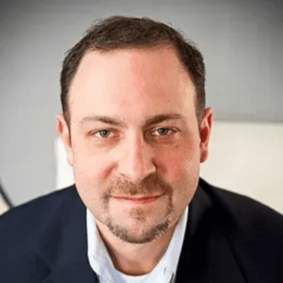 Professional headshot of a man with short brown hair and beard wearing a dark blazer over a light shirt